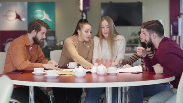 Retrato de cinco jóvenes estudiantes universitarios caucásicos estudiando juntos en la cafetería. Amigos y amigas trabajando en un proyecto estudiantil en un restaurante. Inteligencia, educación, estilo de vida, unidad . — Vídeo de stock