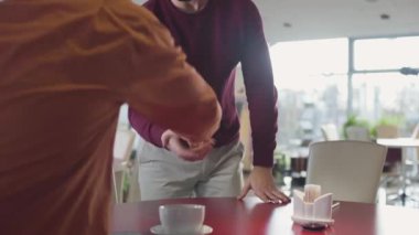 Young bearded Caucasian man coming to the table in cafe and greeting friend. Male fellows talking in restaurant. Friendship, lifestyle, communication.
