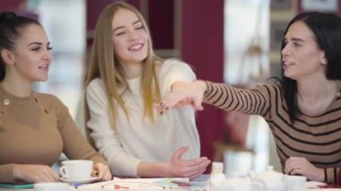 Close-up of group of friendly Caucasian men and women putting hands on top of each other and raising hands up. Unity of cheerful positive friends. Lifestyle, friendship, joy.