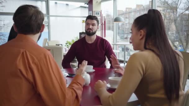 Раздраженные кавказские мужчины и женщины спорят в кафе в солнечный день. Группа друзей конфликтует в ресторане. Бородатый мужчина и блондинка встают и уходят. Конфликт, проблемы со связью . — стоковое видео