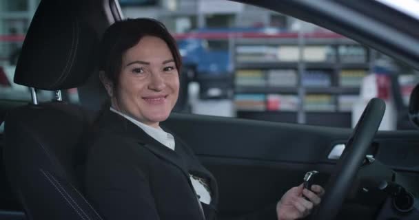 Primer plano de la sonriente mujer de negocios caucásica girando a la cámara y mostrando las llaves de un vehículo nuevo. Cliente femenino satisfecho comprando coche en la sala de exposición. Industria automotriz, riqueza. Sede del cine 4k ProRes . — Vídeos de Stock