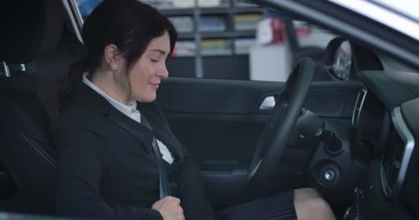 Vue latérale de femme brune caucasienne satisfaite fixant la ceinture de sécurité et le moteur de démarrage dans un véhicule neuf. Portrait de femme d'affaires souriante dans l'automobile. Concessionnaire automobile, style de vie. Siège social Cinema 4k ProRes . — Video