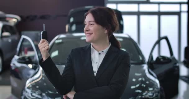 Primer plano de la mujer caucásica alegre mirando las llaves del coche, en la cámara, y sonriendo. Retrato de una exitosa empresaria posando en un concesionario. Riqueza, estilo de vida, industria automotriz, éxito. Sede del cine 4k ProRes . — Vídeo de stock