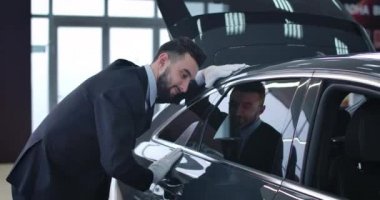 Takım elbiseli, beyaz eldivenli beyaz bir adamın sergi salonunda yeni arabaya dokunuşunun yakın plan görüntüsü. Genç bir satıcı galeride yeni bir aracı inceliyor. Otomobil endüstrisi. Sinema 4k Prores Merkezi.