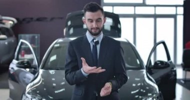 Arabanın anahtarlarını kusan ve kameraya gülümseyen genç beyaz adamın portresi. Başarılı bir iş adamı galeride yeni bir araç satın alıyor. Otomobil endüstrisi, satın alma. Sinema 4k Prores Merkezi.