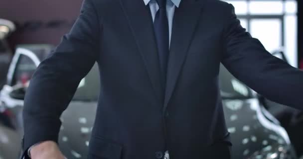 Крупный план неузнаваемого кавказского бизнесмена в костюме, скрещивающего руки. Молодой успешный человек, стоящий в автосалоне перед новым черным автомобилем. Штаб-квартира кинотеатра 4k ProRes . — стоковое видео