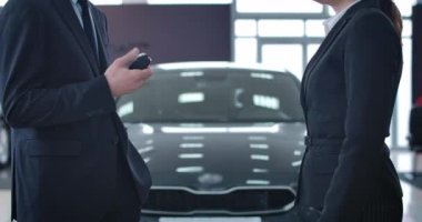 Beyaz bir erkek araba satıcısı yeni aracın anahtarlarını otomobilin önünde tanınmayan genç bir bayana veriyor. İş kadını galeriden araba alıyor. Otomobil endüstrisi, ticaret. Sinema 4k Prores Merkezi.