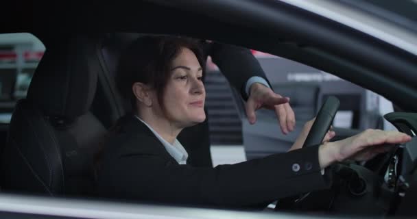 Detailní pohled na vážnou bělošskou brunetku, která poslouchá obchodníka, jak sedí v autě. Dospělá obchodnice si vybrala auto v prodejně aut. Cinema 4k Prores Hq. — Stock video