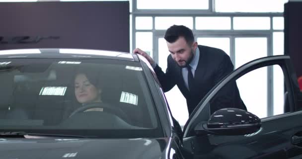 Positive handsome male dealer consulting successful businesswoman sitting on drivers seat. Caucasian man selling new vehicle to confident adult woman. Cinema 4k ProRes HQ. — Stock Video