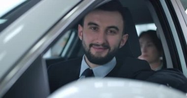 Yolcuyla arabada oturan ve kameraya bakan pozitif beyaz bir adamın portresi. Takside çalışan ya da özel şoför olarak gülümseyen profesyonel bir şoför. Sinema 4k Prores Merkezi.