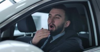 Sürücü koltuğunda oturan ve esneyen yorgun beyaz adamın yakın plan portresi. Tükenmiş özel şoför ya da taksi şoförü müşteri ya da şefi bekliyor. Sinema 4k Prores Merkezi.
