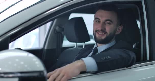 Egy közeli kép elégedett kaukázusi fiatalemberről, aki autóban pózol a vezetőülésen. Pozitív jóképű férfi, aki új autót vesz a kereskedésben. Mozi 4k Prores Hq. — Stock videók