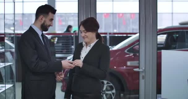 一个兴奋的高加索女人从新的红色轿车上从男性经销商那里得到钥匙并做出胜利姿态的画像。满意的女客户在经销商处购买汽车。电影4k Prores Hq. — 图库视频影像