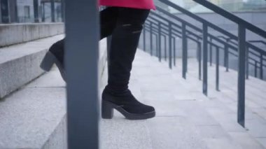 Camera following female legs in high boots walking down the stairs. Woman strolling in city. Lifestyle, leisure.