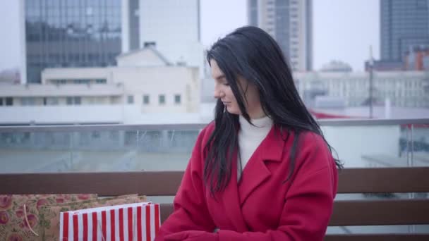 Retrato de la joven positiva mujer caucásica abriendo paraguas colorido como sentado en la ciudad bajo la lluvia ligera con bolsas de compras. Encantadora dama disfrutando de un día lluvioso al aire libre. Felicidad, estilo de vida, ocio . — Vídeo de stock