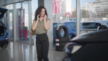 Yeni arabaya atlayıp zıplayan, heyecanlı, beyaz bir genç kadın. Araba galerisinden araba alan kıvırcık saçlı mutlu bir kadın. Otomobil endüstrisi, başarı, satın alma.