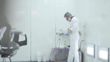 Profesyonel beyaz erkek araba boyacısı koruyucu iş kıyafeti giyiyor. İş yerinde beyaz iş elbisesi giymiş bir adamın portresi. Otomobil endüstrisi, oto tamirhanesi, araç bakımı.