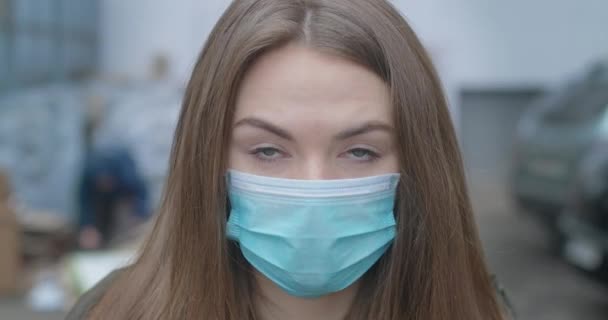 Primer plano de la cara de la chica en máscara protectora mirando a la cámara. Joven mujer morena hermosa con ojos grises al aire libre en la ciudad. Pandemia, medicina, Covid-19. Sede del cine 4k ProRes . — Vídeos de Stock