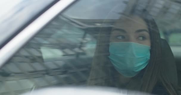 Ung brunett kvinna i skyddande mask nysningar och hosta som sitter på förarsätet. Porträtt av en vacker sjuk flicka i bilen. Influensa, infektion, coronavirus. Cinema 4k Prores Hq. — Stockvideo