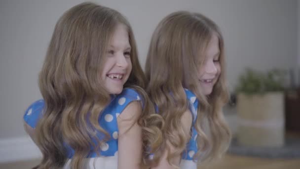 Caméra approchant des visages de deux sœurs jumelles identiques parlant et riant. Brunette filles gaies en bleu pointillé robes reposant ensemble à la maison. Famille, mode de vie, unité .