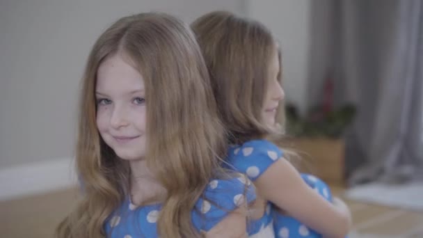 Cámara moviéndose de izquierda a derecha alrededor de dos hermanas gemelas idénticas en vestidos de puntos azules similares. Hermanas morenas con ojos grises posando en el interior los fines de semana. Unidad, felicidad, estilo de vida . — Vídeo de stock