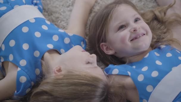 Extreme close-up van vrolijke blanke tweelingzussen die praten en lachen. Bovenaanzicht van vrolijke kinderen die binnen op zacht tapijt liggen en roddelen. Geluk, vreugde, vrije tijd, eenheid. — Stockvideo