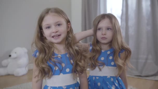 Happy and sad Caucasian twins talking indoors. Portrait of joyful girl and upset child at home. Difference in temperament type, unity, family. — Stock Video