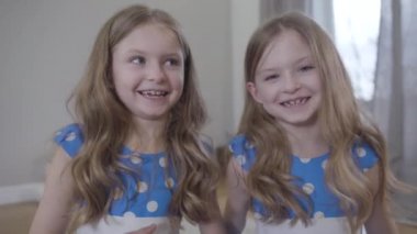 Close-up portrait of two cute Caucasian sisters waving at camera. talking and smiling. Front view of cheerful little twins having video chat. Joy, lifestyle, beauty.
