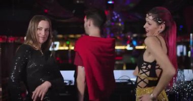 Middle shot of young beautiful Caucasian PJs dancing seductively as male DJ mixing music on controller. Three joyful people entertaining in night club on stage. Cinema 4k ProRes HQ.