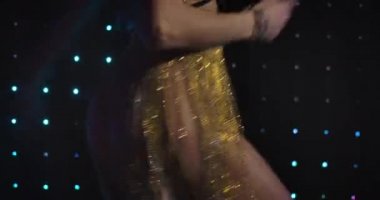 Unrecognizable seductive Caucasian woman in sparkling dress dancing at the background of lights on black wall. Professional female go go dancer performing in night club. Cinema 4k ProRes HQ.
