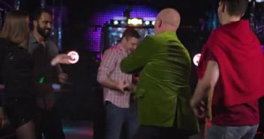 Back view of stylish mature Caucasian man in green jacket dancing in night club surrounded by young people. Cheerful company resting in disco. Leisure, entertainment, lifestyle. Cinema 4k ProRes HQ.