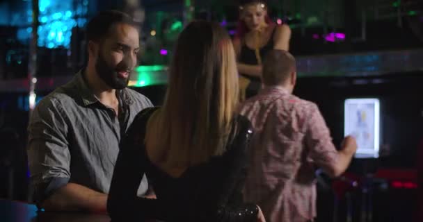 Un giovane uomo affascinante del Medio Oriente che parla con una donna caucasica irriconoscibile nel night club. Gioiosa coppia multirazziale che riposa accanto al bancone del bar in discoteca. Cinema 4k ProRes HQ . — Video Stock