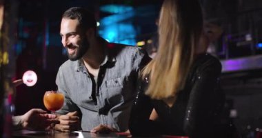 Cheerful young Middle Eastern man taking cocktail and talking with bartender in night club. Happy handsome bearded guy hanging out in disco. Lifestyle, entertainment, joy. Cinema 4k ProRes HQ.