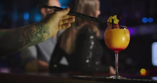 Чоловіча кавказька рука з татуюванням готує коктейлі в нічному клубі. Відвідувачі стоять на задньому плані. Професійний бармен наливає на прилавок склянку з напоєм. Фільм 4k Prores Hq. — стокове відео