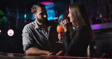 Young attractive Caucasian woman drinking cocktail and talking with handsome Middle Eastern man in night club. Pretty elegant girl flirting with confident guy. Cinema 4k ProRes HQ.