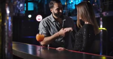 Portrait of young Middle Eastern man and Caucasian woman meeting each other in night club. Cheerful couple standing next to bar counter with cocktail and talking. Cinema 4k ProRes HQ.