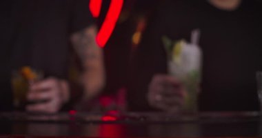 Two male bartenders putting glasses with cocktails on bar counter. Close-up of mixed drinks in night club. Cinema 4k ProRes HQ.
