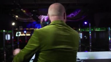 Close-up of elegant senior Caucasian man in red bow tie and green jacket posing at workplace in night club. Active elderly DJ looking at camera and smiling. Lifestyle, occupation, entertainment.