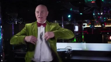 Joyful mature Caucasian man in green jacket spinning and singing next to music controller. Senior male DJ working in night club. Occupation, hobby, lifestyle, entertainment.