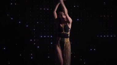 Young seductive Caucasian woman dancing at the background of black wall with lights. Female go go dancer with tattoo on hand and red hair working in night club. Occupation, entertainment, lifestyle.