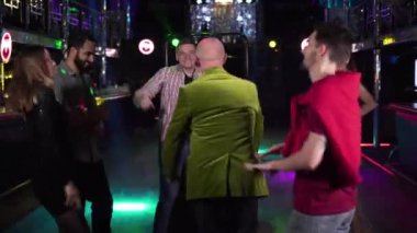 Group of young multi-ethnic people dancing around cheerful elderly man in night club. Positive men and women resting in disco. Relaxation, leisure, lifestyle, entertainment.