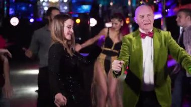 Joyful elderly Caucasian man and young woman dancing in night club. Positive people of different ages resting in the evening in disco. Fun, joy, lifestyle.