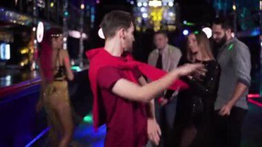 Portrait of young handsome Caucasian brunette man dancing in night club. Positive guy spending evening in disco with friends having fun at the background. Joy, lifestyle, relaxation.