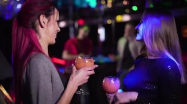 Focus changes from young Caucasian women talking at the foreground to handsome men standing at the background in night club. Girls and guys flirting in the evening. Leisure, lifestyle, night life.