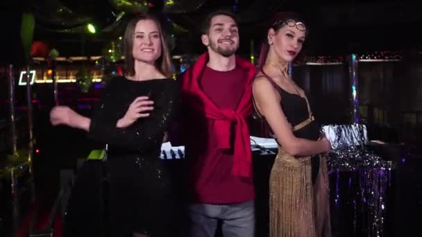 Young Caucasian beautiful women and handsome man posing in night club. Positive male DJ hugging cheerful female go go dancers standing in disco with hands crossed. Lifestyle, resting, entertainment. — Stok video