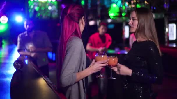 Charmante blanke vrouwen dansen met cocktails aan de bar balie wanneer mannen van verschillende etniciteiten naar hen toe komen. Positieve jongeren die 's avonds in de nachtclub rondhangen. — Stockvideo