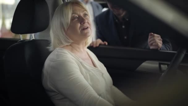 Porträtt av en fin mogen vit kvinna som sitter på förarsätet och pratar med bilhandlare. Självsäker äldre dam väljer fordon i återförsäljaravtal. bilindustri, köp, handel. — Stockvideo