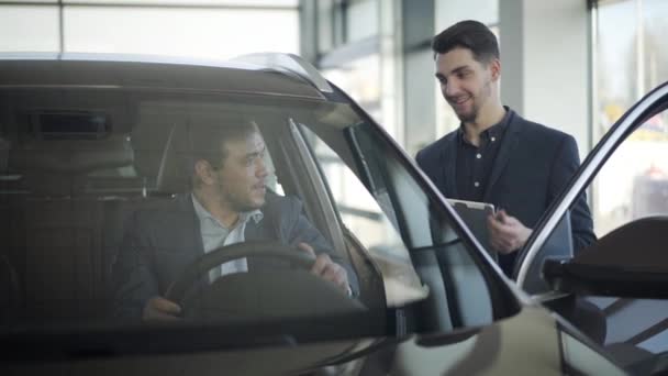 Hombre sonriente comerciante caucásico dando llaves de coche para hombre de negocios adulto sentado en el asiento del conductor. Cliente exitoso comprando automóvil en concesionario. Negocios, estilo de vida, riqueza, éxito . — Vídeo de stock