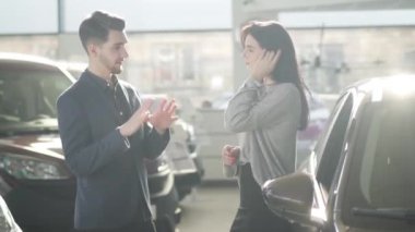 Yakışıklı beyaz araba satıcısının galeride güzel bir bayan müşteriyle konuşup elini sıktığının yan görüntüsü. Güneş ışığında bayilikte durup gülümseyen pozitif insanlar..