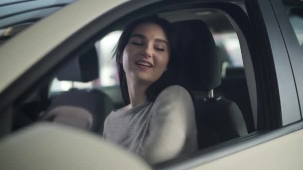 Portrait de jeune femme caucasienne attrayante regardant la caméra comme assis sur le siège du conducteur dans une nouvelle voiture. Joyeux succès femme d'affaires posant dans son automobile dans le concessionnaire. Mode de vie, joie, bonheur . — Video